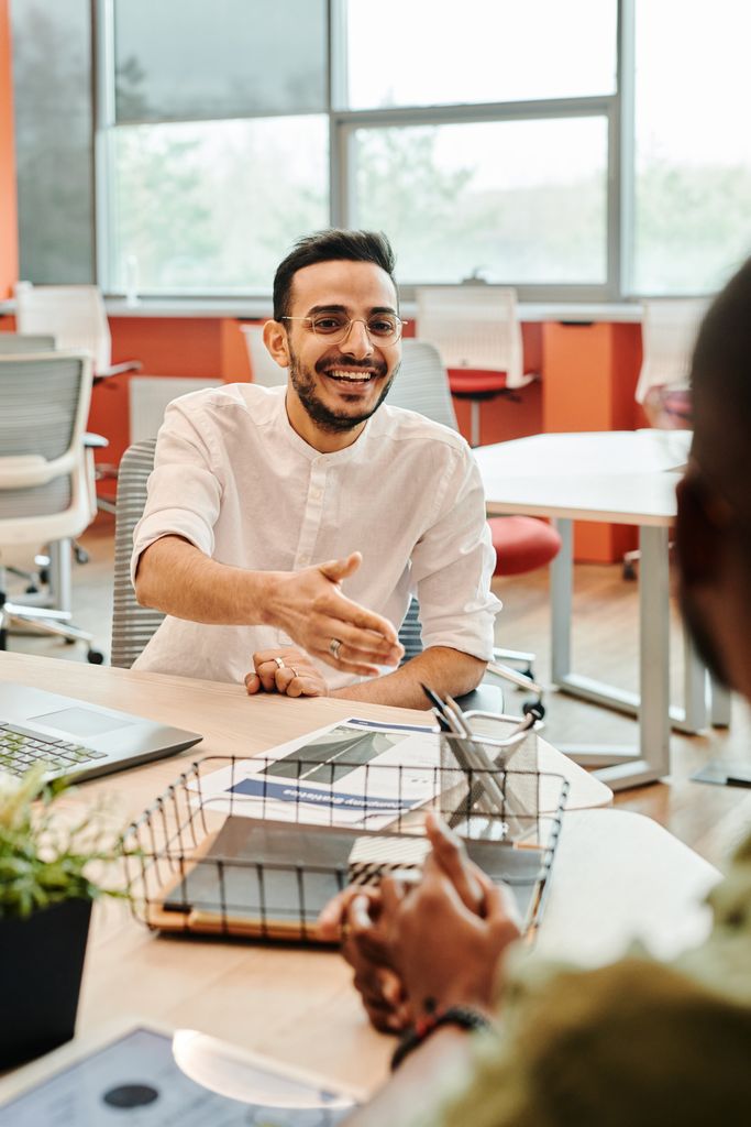 A cheerful businessman extends a handshake in a modern office environment, promoting a positive atmosphere.