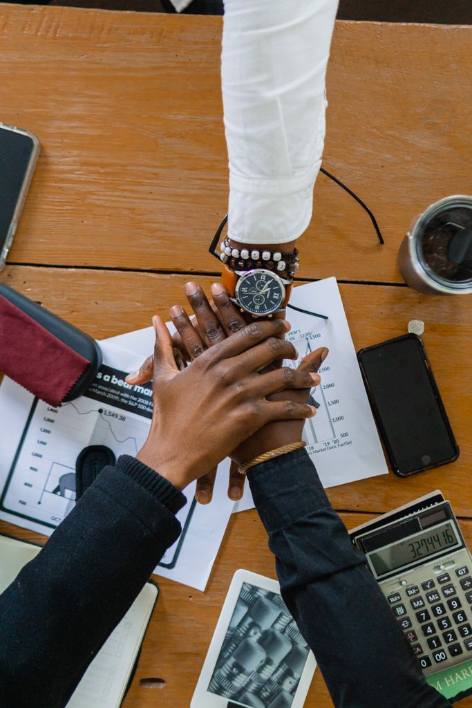 Top view of diverse hands stacked on office desk, symbolizing teamwork and collaboration.